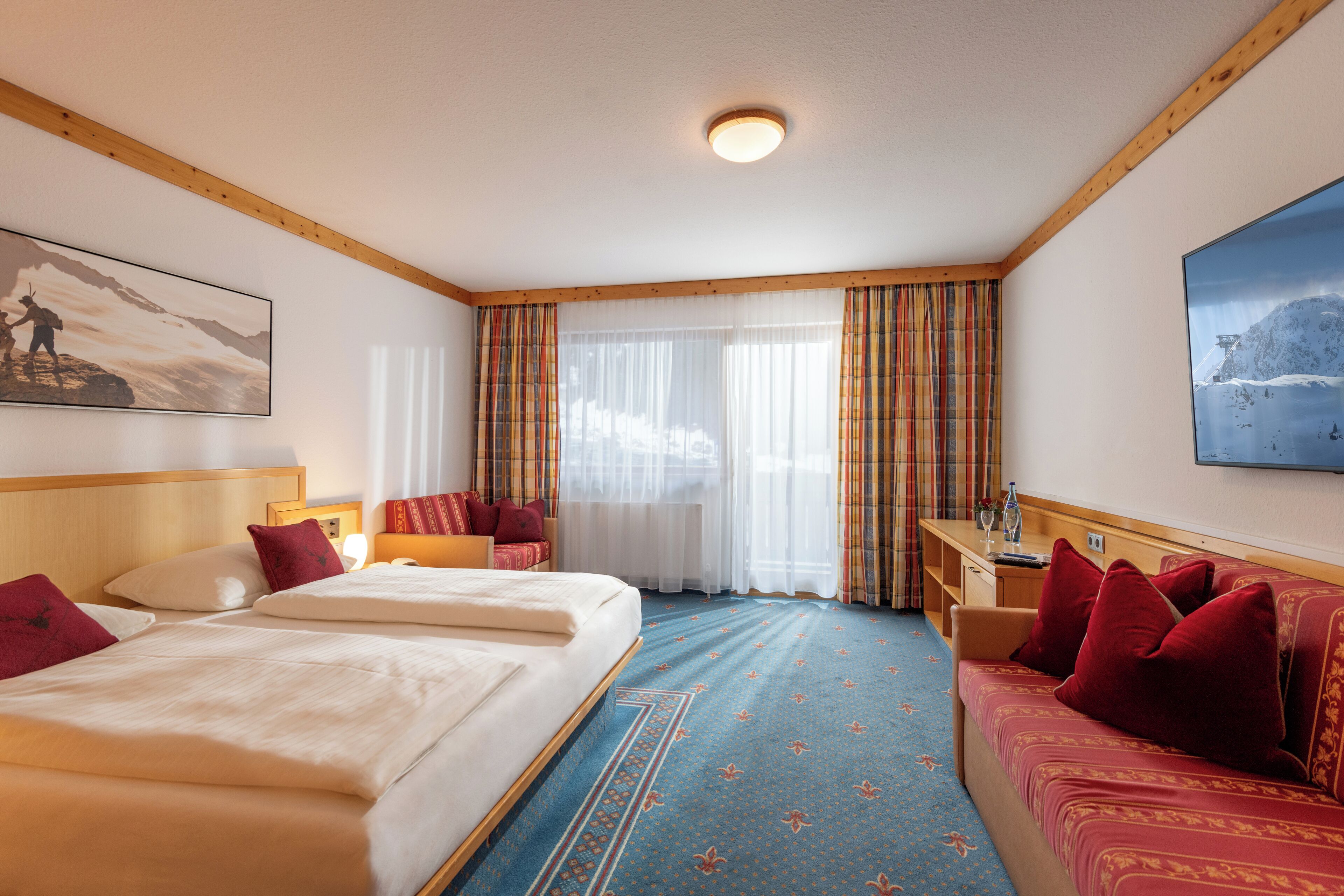 A hotel room with a large bed, a sofa, a desk, and a window with curtains.