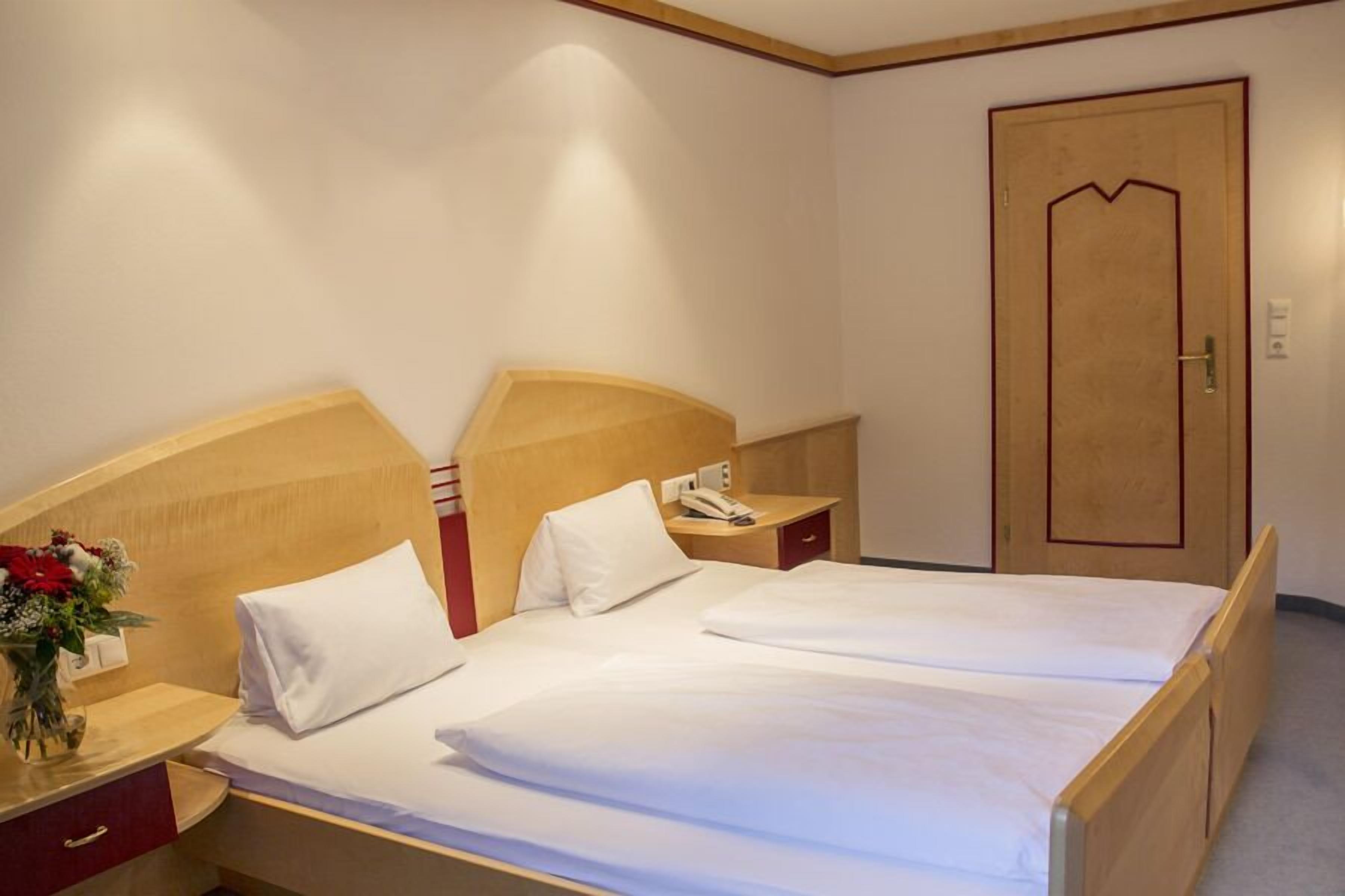 A hotel room with a wooden bed, white linens, a bedside table with a phone, and a wooden door.