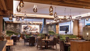 A modern restaurant with multiple seating areas, including a bar and a dining room with tables and chairs. - Alpensporthotel Mutterberg (Neustift Im Stubaital)
