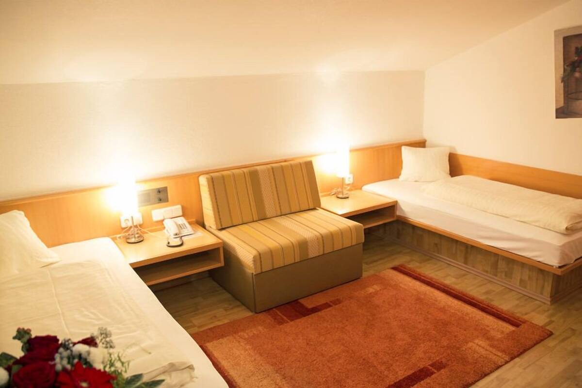 Une chambre d’hôtel avec un lit, un canapé, une table de chevet avec une lampe et une petite table avec un téléphone.