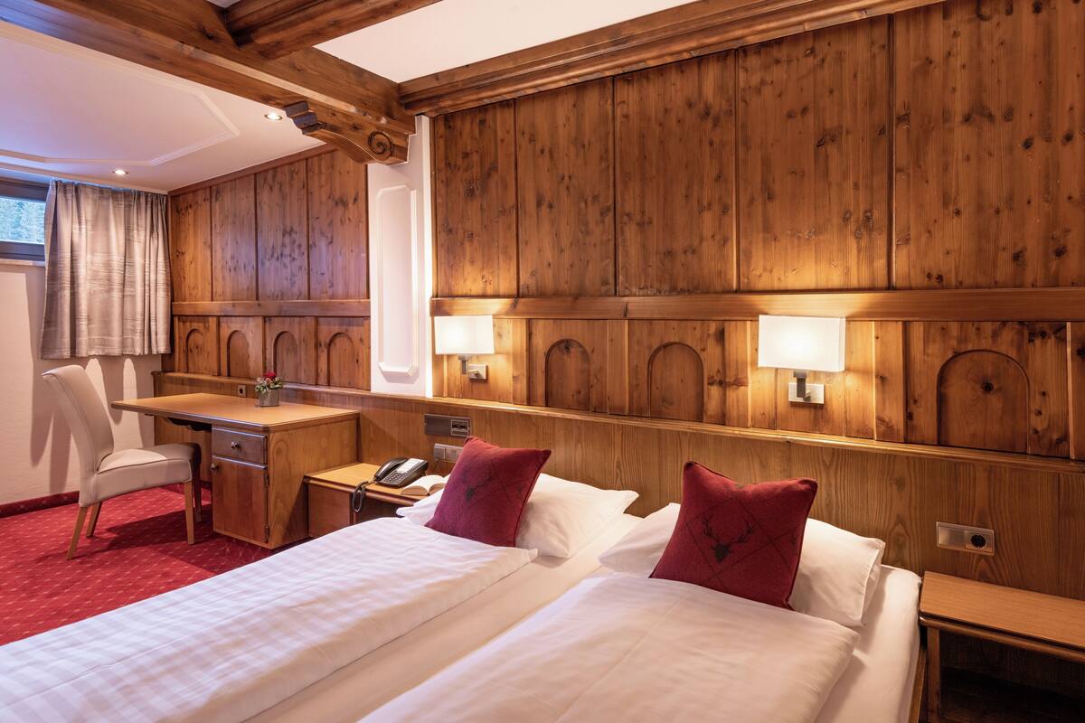 Une chambre d’hôtel avec des lambris en bois, un bureau avec un téléphone, deux lits avec des oreillers rouges et une chaise.