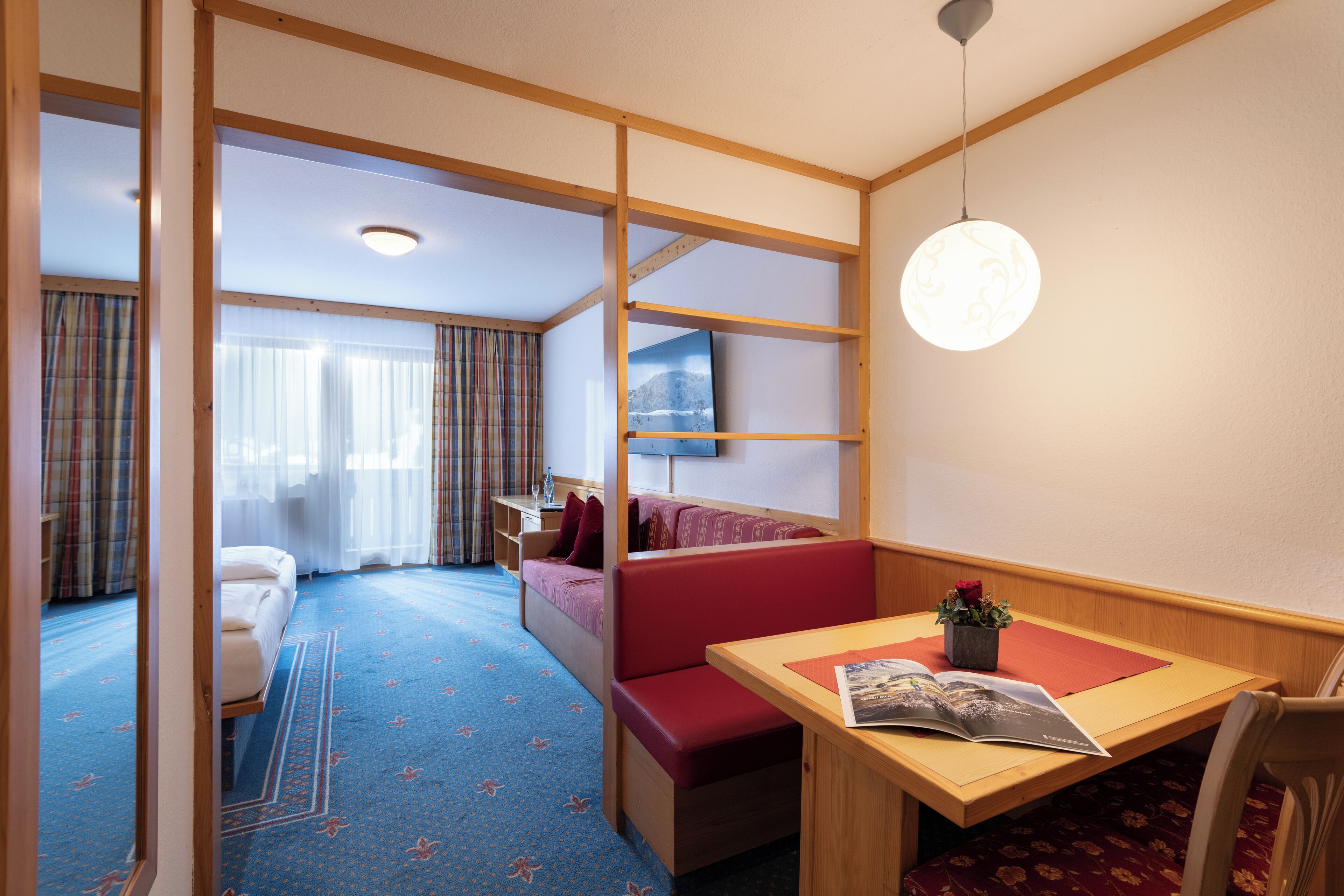 Een hotelkamer met een bed, een slaapbank, een eettafel en een bijzettafeltje met een plant.