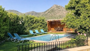 Una piscina con sillas de descanso, una estructura de madera y montañas al fondo.