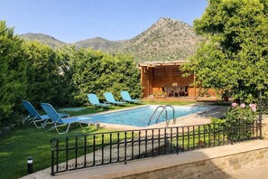Ein Pool mit Liegestühlen, einer Holzkonstruktion und einem Bergpanorama.