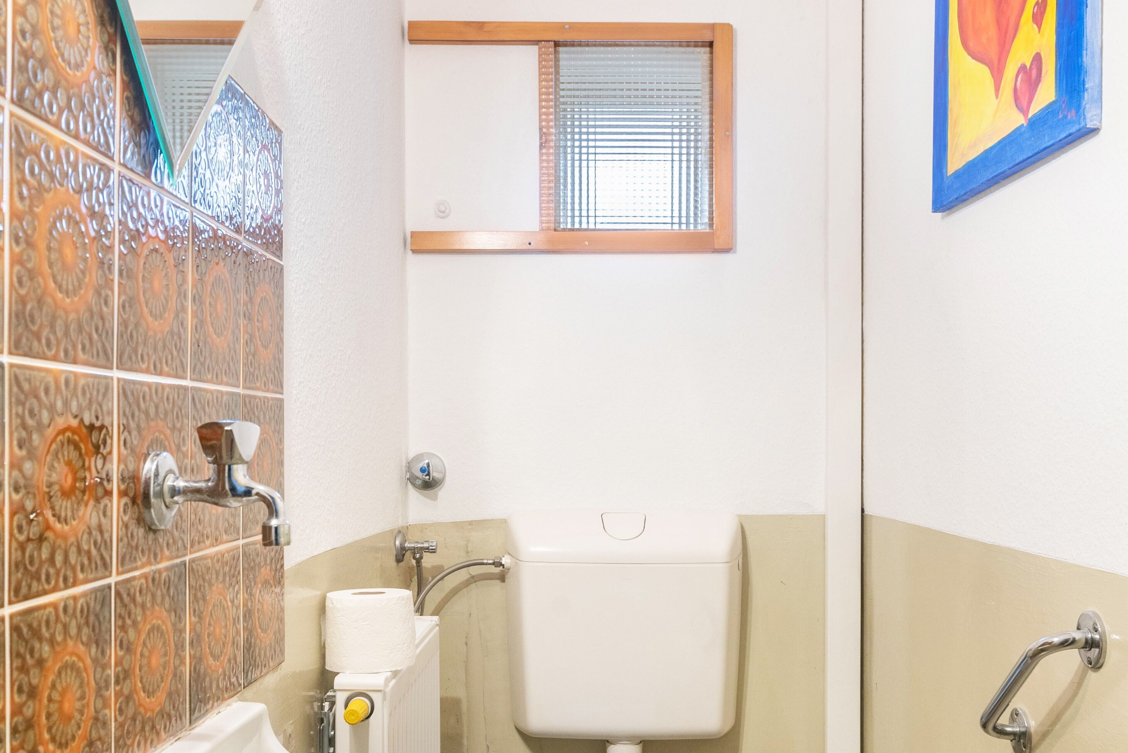 A bathroom with patterned tiles, a toilet, a sink, a window, and a shower.