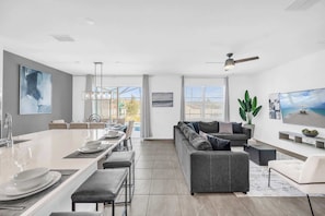 A modern kitchen with a dining area, a gray sofa, and a TV. - Upstay Vibrant Home w Themed Rooms Pool Games (Kissimmee)