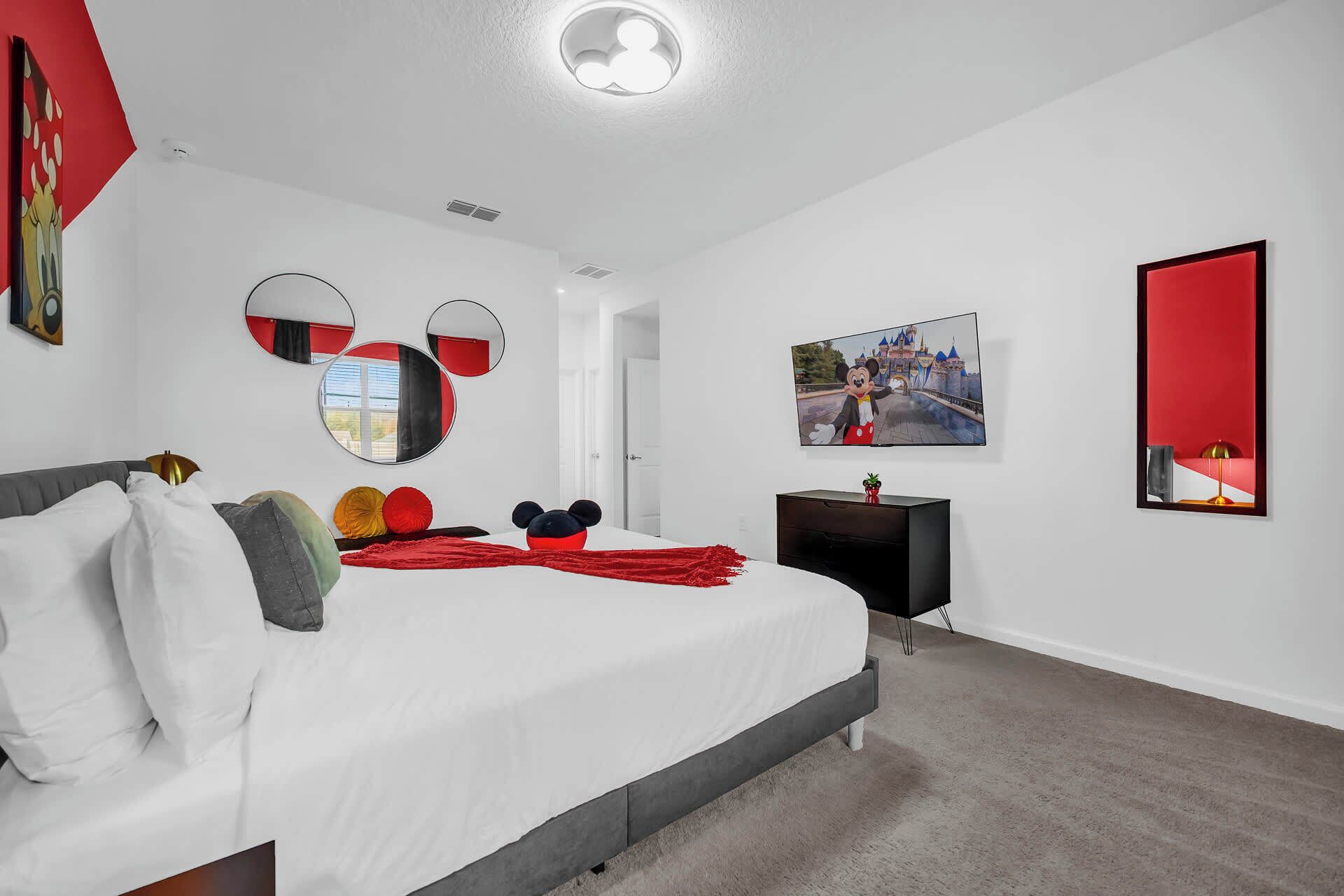 A modern bedroom with a large bed, a flat-screen TV, and a Mickey Mouse-themed decor.