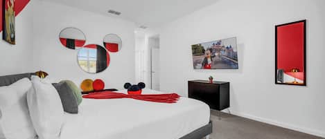 A modern bedroom with a large bed, a flat-screen TV, and a Mickey Mouse-themed decor.