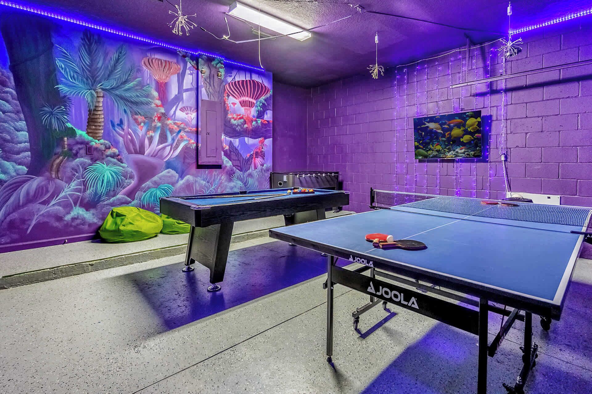 A room with two pool tables, a mural with tropical and marine themes, and a fish tank on the wall.