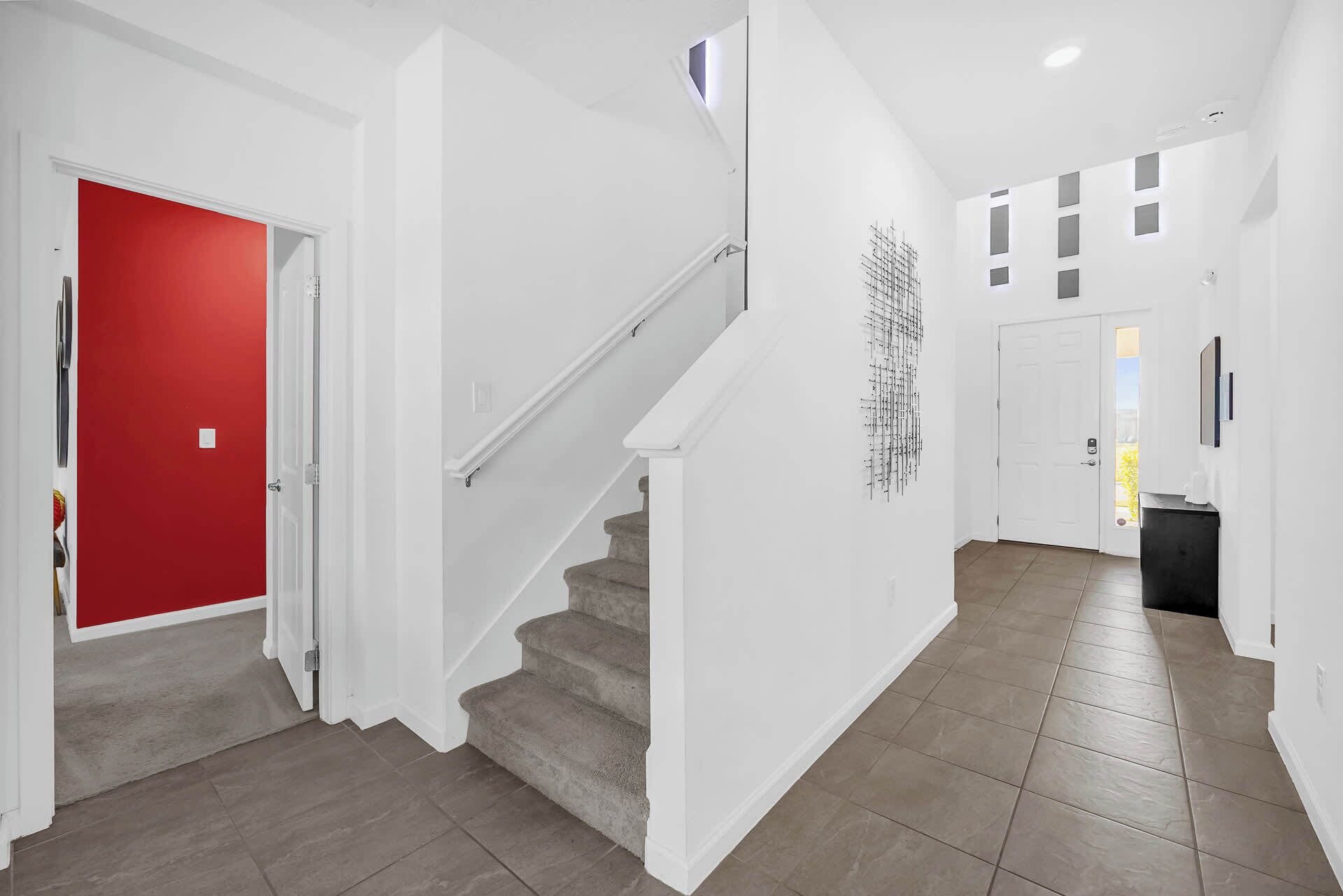 A modern hallway with a red door, a staircase, and a wall-mounted art piece.