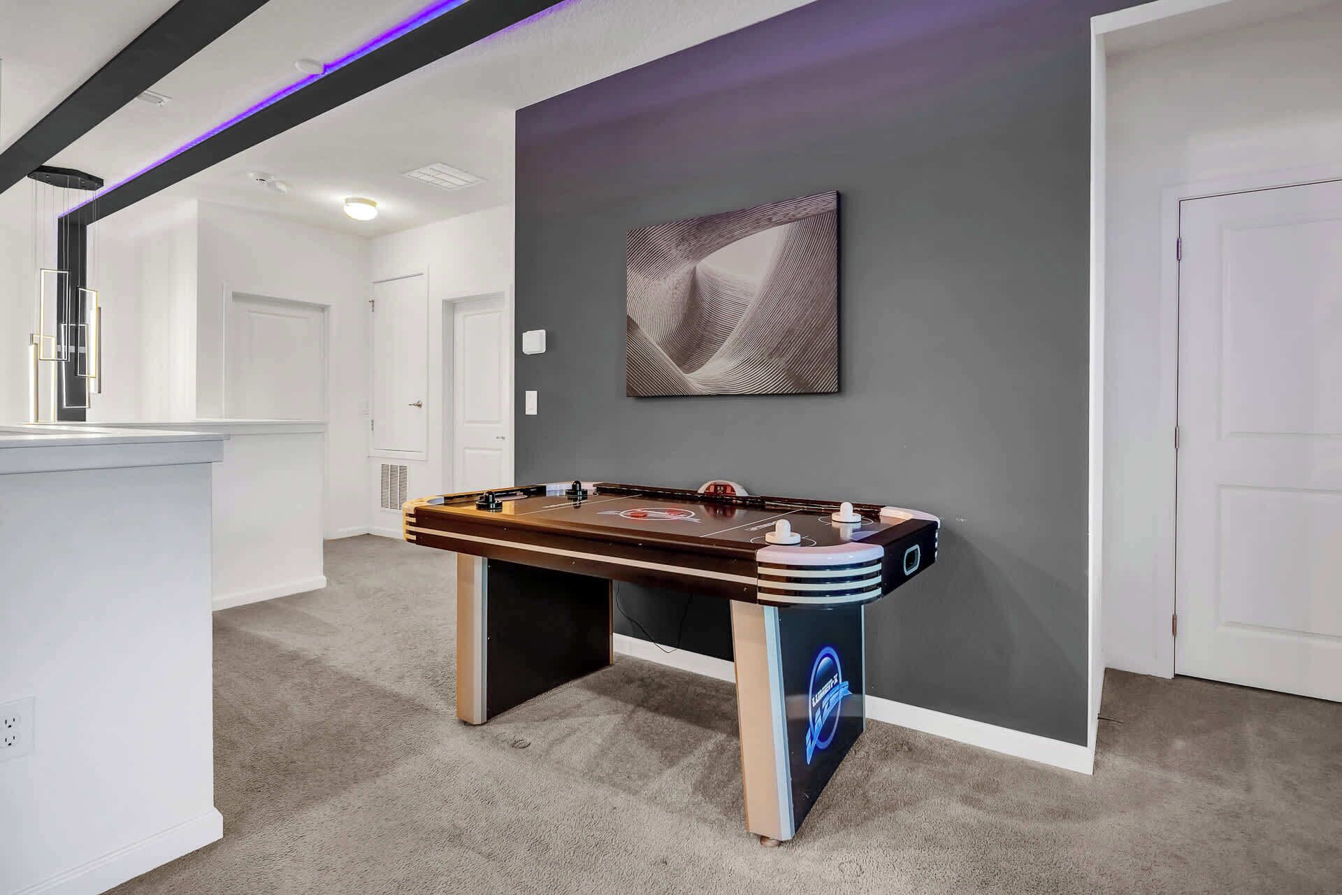 Una habitación moderna con mesa de fútbol, un cuadro en la pared y una puerta blanca.