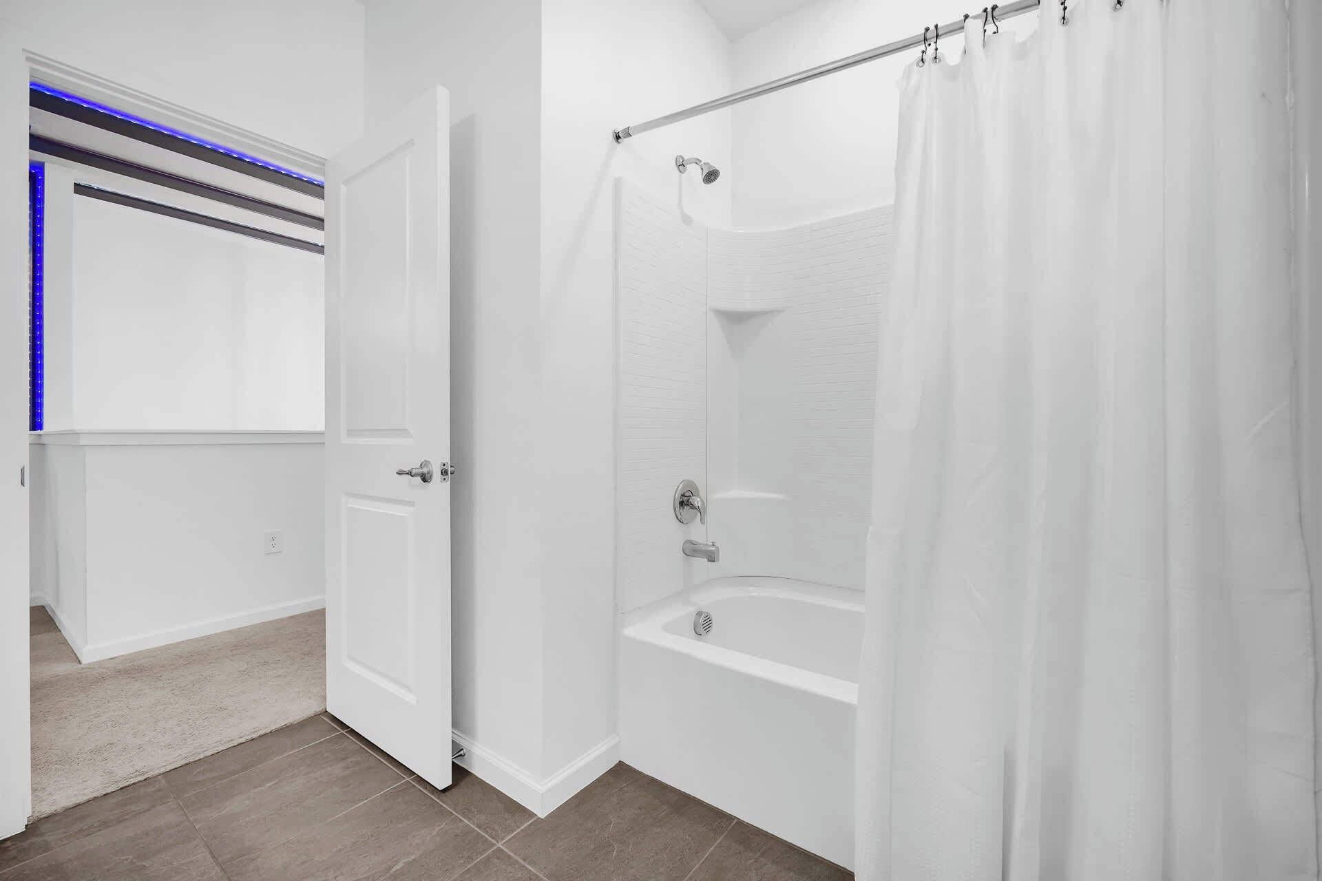 A modern bathroom with a walk-in shower, a bathtub, and a door with a blue LED light strip.