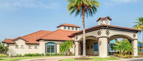 A two-story building with a red-tiled roof, a central entrance with an archway, and a palm tree in the foreground.