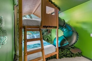 Ein Stockbett mit Rutsche, grüne Wände und einem tropischen Wandgemälde.
