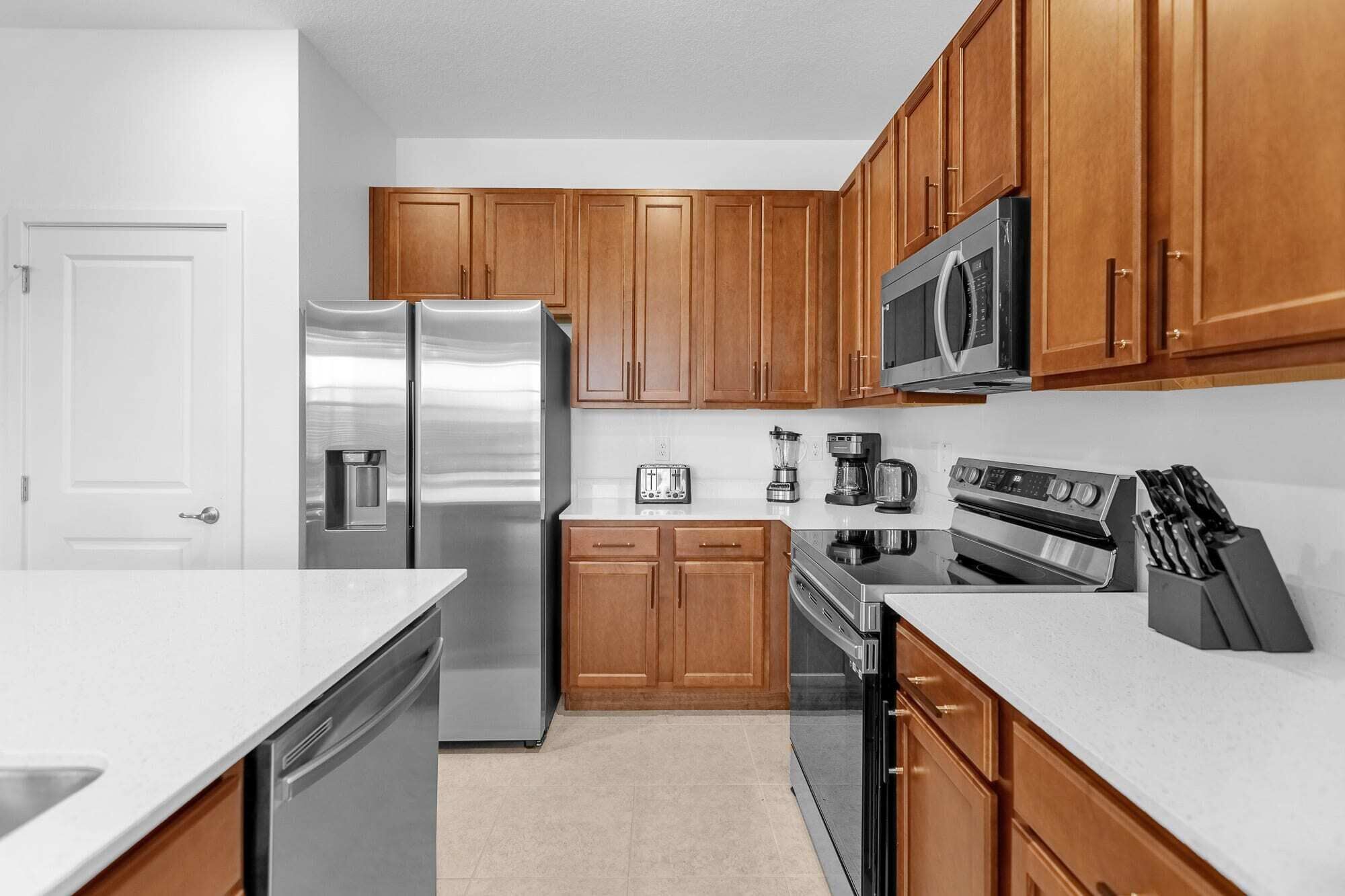 A kitchen with wooden cabinets, stainless steel appliances, a microwave, toaster, coffee maker, and a knife block.