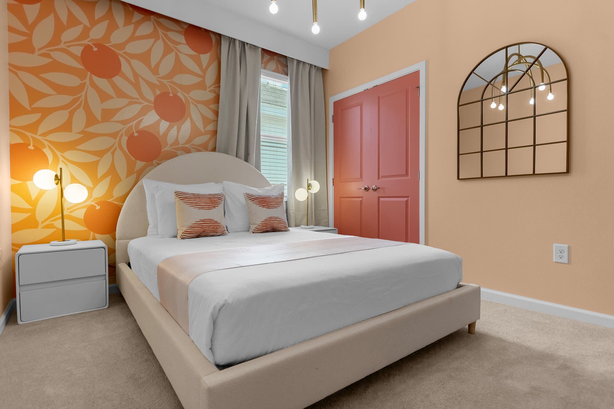 A bedroom with a bed, nightstands, a wall-mounted light fixture, a door, and a window with curtains.