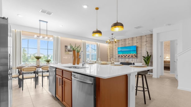 Una cocina moderna con una isla grande, electrodomésticos de acero inoxidable, iluminación colgante y vistas al exterior.