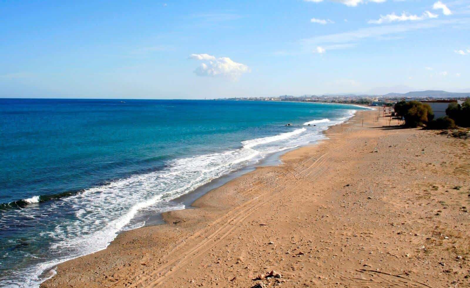 A beach with a clear view of the ocean and distant cityscape.