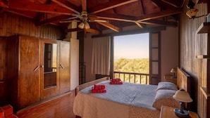 Quarto de madeira com uma cama, um guarda-roupa, um ventilador de teto e uma janela com vista.