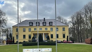 Keltainen rakennus, jossa on tiilikatto, ja sen ympärillä on hyvin hoidettu nurmikko ja puita.