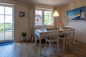Comedor con una mesa, sillas, ventana con cortinas, un cuadro en la pared y una planta en maceta.