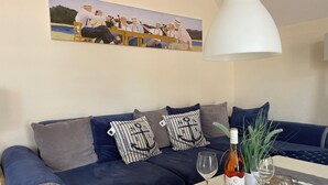 A living room with a blue sofa, striped pillows, a table with a bottle of wine, a glass, and a lamp.