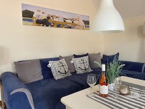 A living room with a blue sofa, striped pillows, a table with a bottle of wine, a glass, and a lamp.