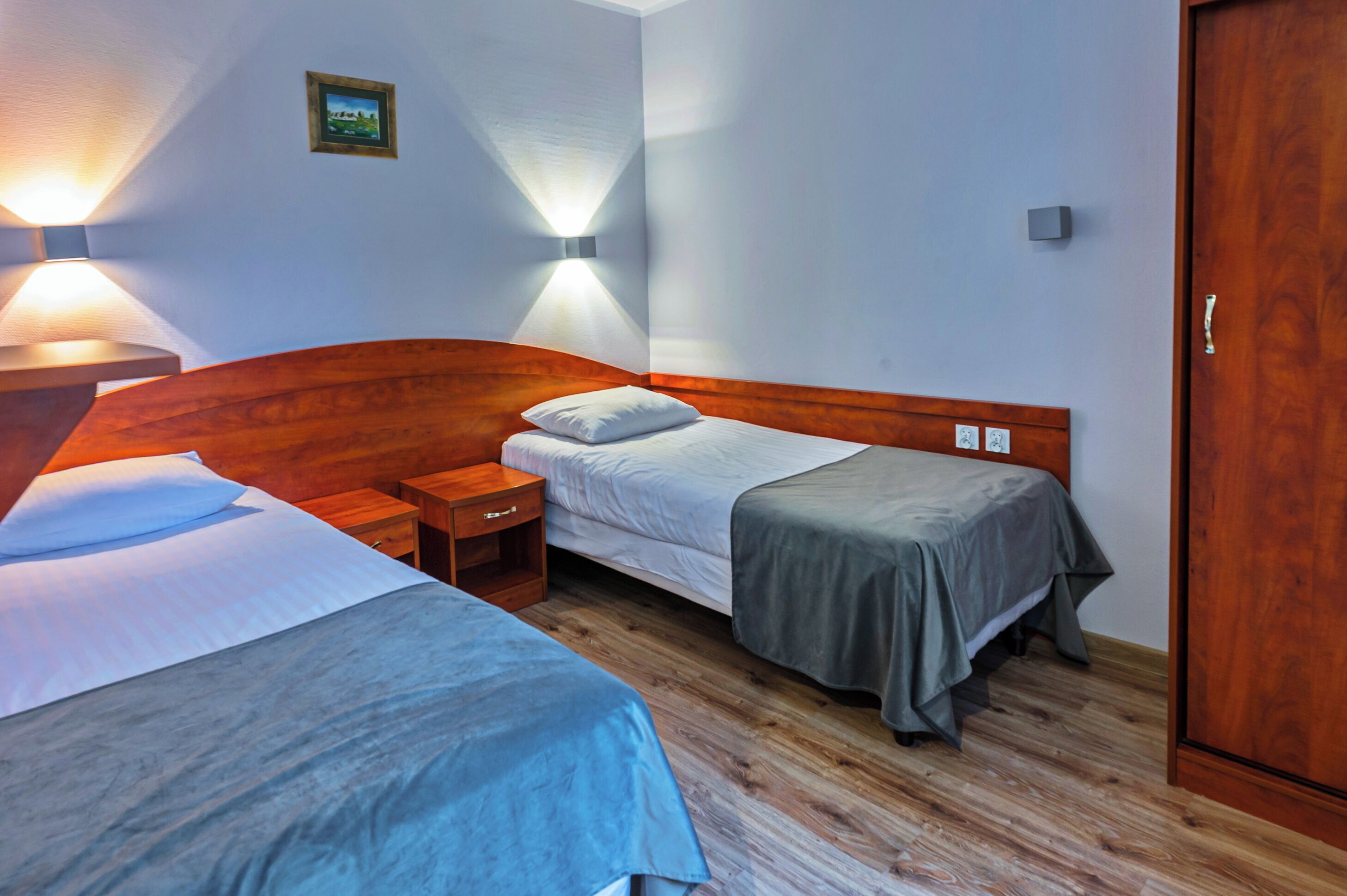 A hotel room with two beds, wooden headboards, bedside tables, and wall-mounted lamps.