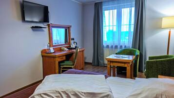 A hotel room with two beds, a desk with a telephone, a chair, a television mounted on the wall, and a window with curtains.