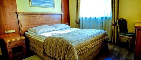 Una habitación de hotel con una cama grande, cabecera de madera, una mesita de noche, una silla y un cuadro en la pared.