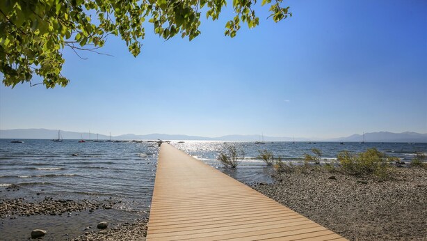 Une promenade en bois mène à une côte rocheuse où se trouvent des bateaux sur l’eau.