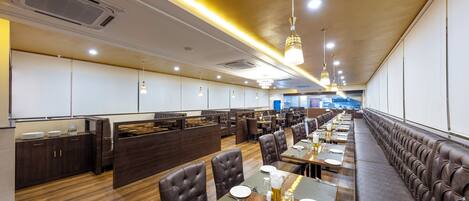 A spacious restaurant with long tables and booths, wooden flooring, and modern lighting fixtures.