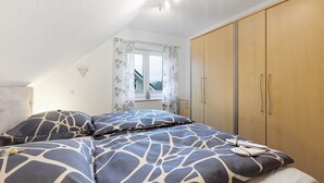 Un dormitori amb un llit, un armari i una finestra amb cortines.