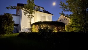 Una casa amb un teulat inclinat, una xemeneia visible i la lluna al cel.