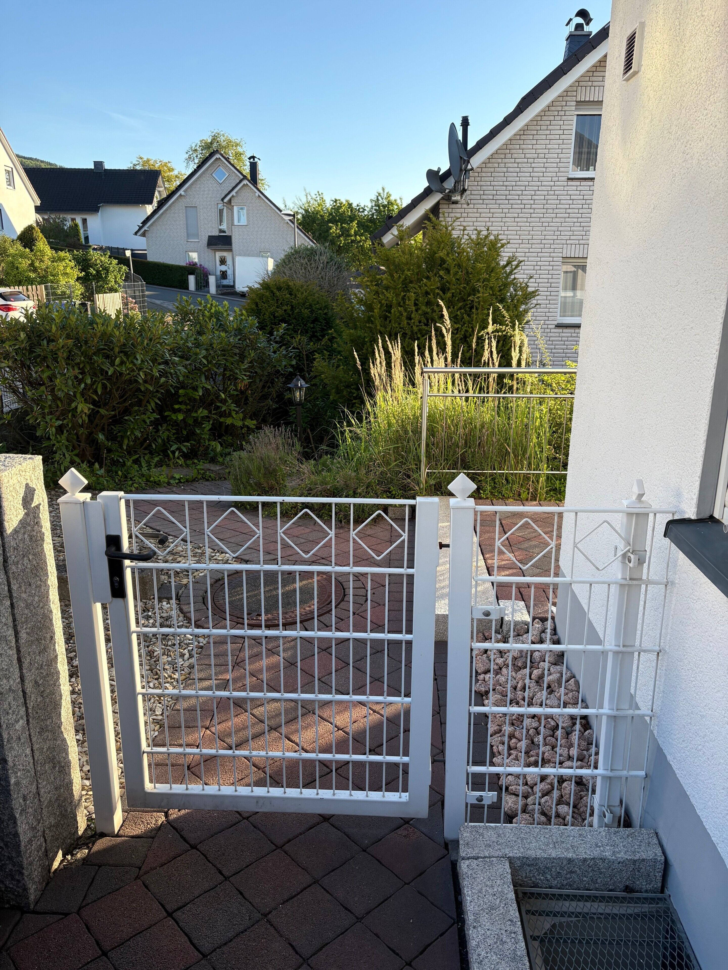 A gated entrance with a metal gate, a paved pathway, and a white building with a brick facade.