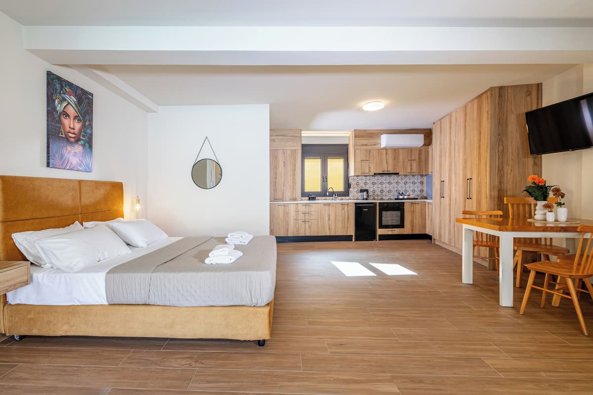 A modern hotel room with a bed, a dining area, and a kitchen.