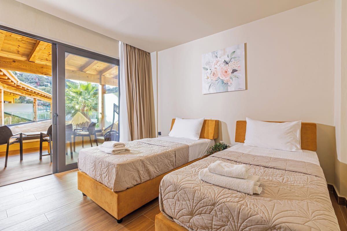 A hotel room with two beds, a large sliding glass door leading to an outdoor area, and a painting on the wall.