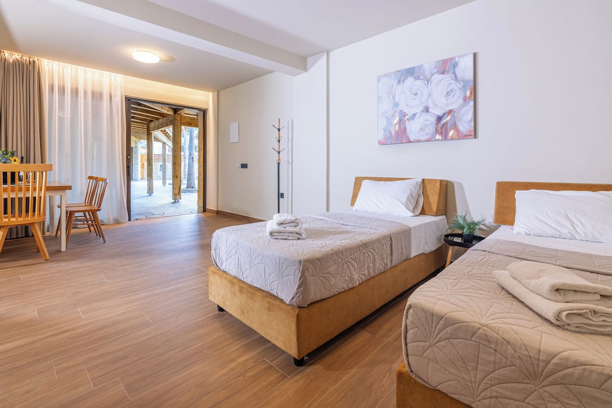 A hotel room with two beds, wooden flooring, a dining area with chairs, and a painting on the wall.