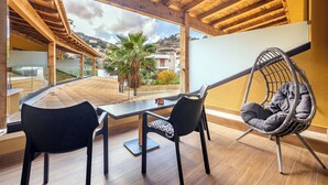 Ein modernes Zimmer mit Holzboden, einem Balkon mit Blick auf Häuser und Hügel, einem Esstisch mit Stühlen und einem Hängesessel.