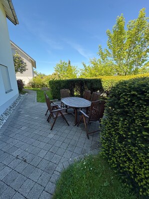 A patio with a table and chairs, surrounded by greenery and a hedge. - Apartment Ruhrtal – Central Location in Bestwig, Supermarkets Nearby, Garden Access, Fiber Internet (Bestwig)