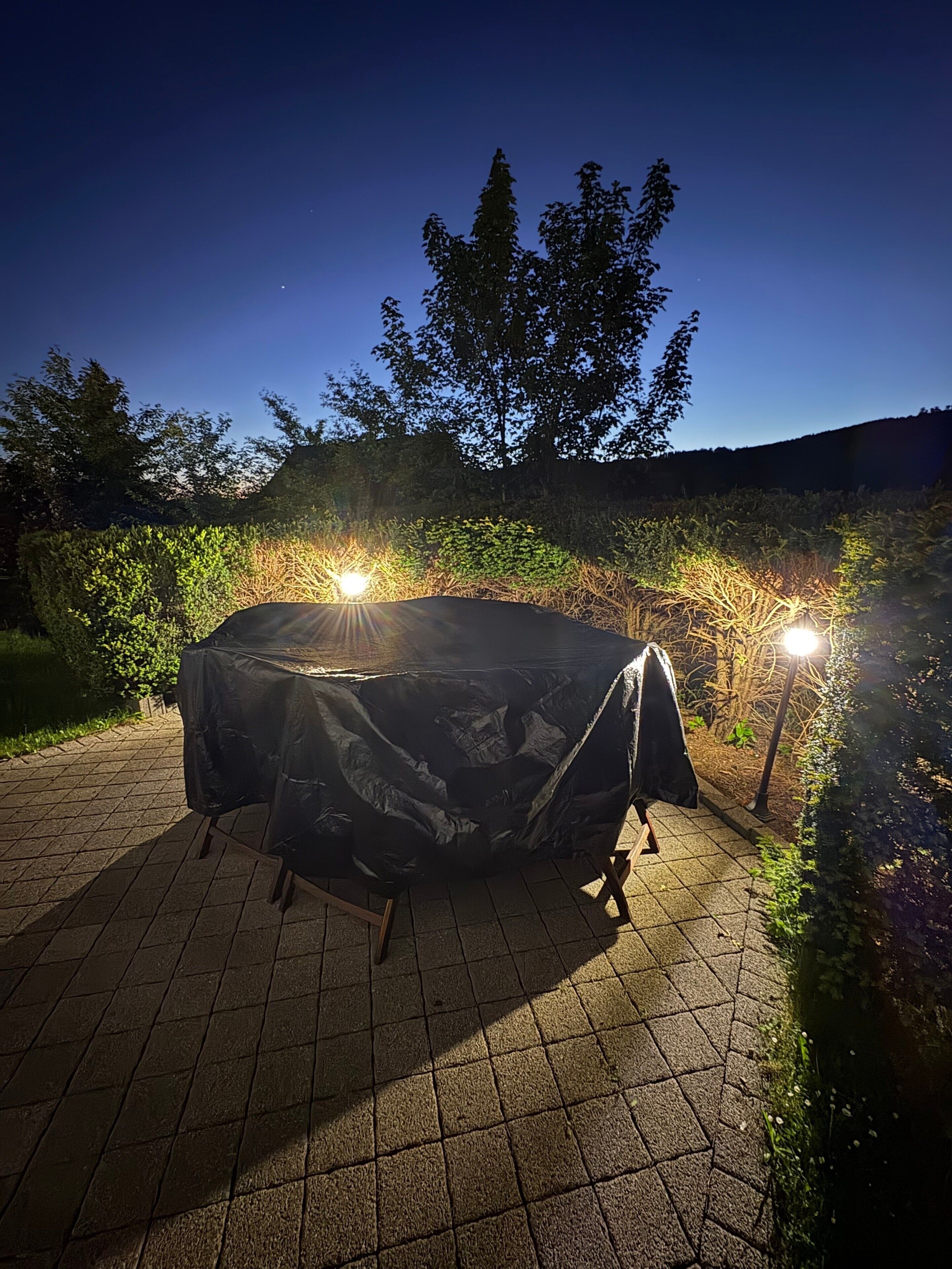 An outdoor dining area with a covered table and two lamps.