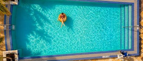 Una piscina rectangular con agua cristalina, rodeada por un solárium con baldosas.