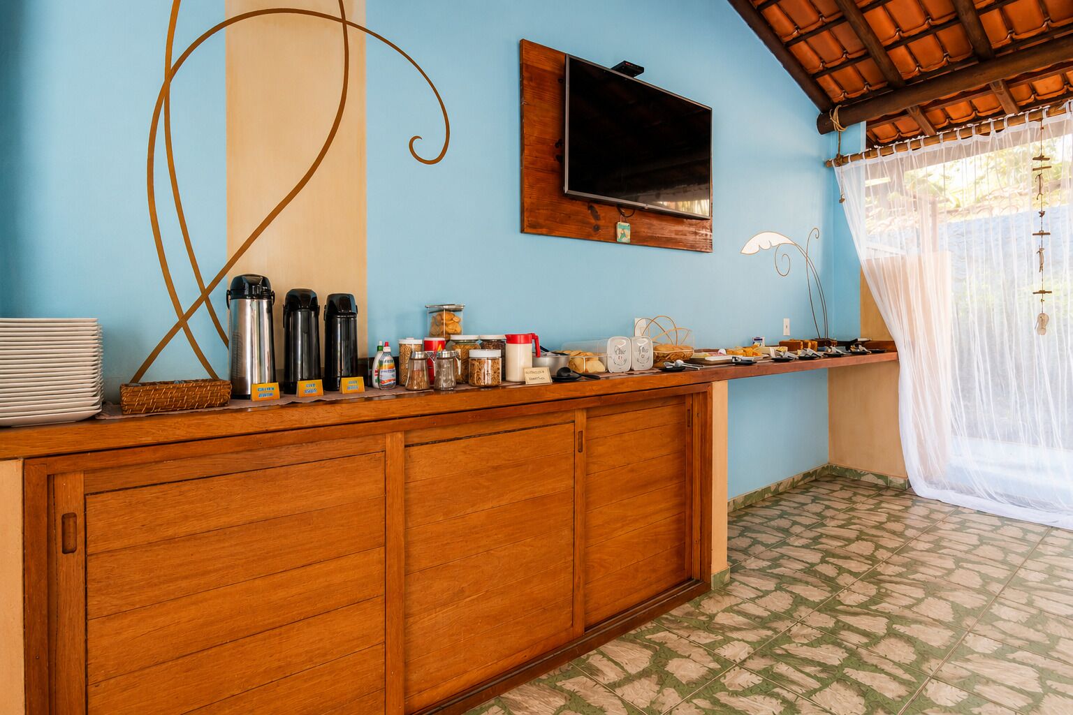 Una habitación con mostrador de madera, televisor montado en la pared y ventana con cortina.
