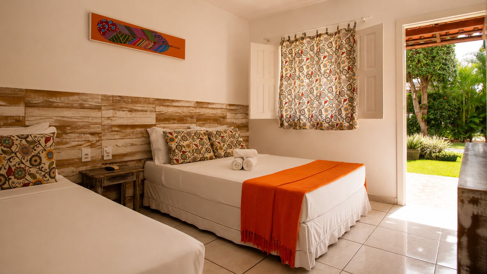 A hotel room with a bed, a nightstand, a painting on the wall, and a view of the garden through an open door.