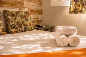 A neatly made bed with rolled white towels, a patterned pillow, and a small bedside table with a remote control. - Pousada Universo Arraial (Porto Seguro)