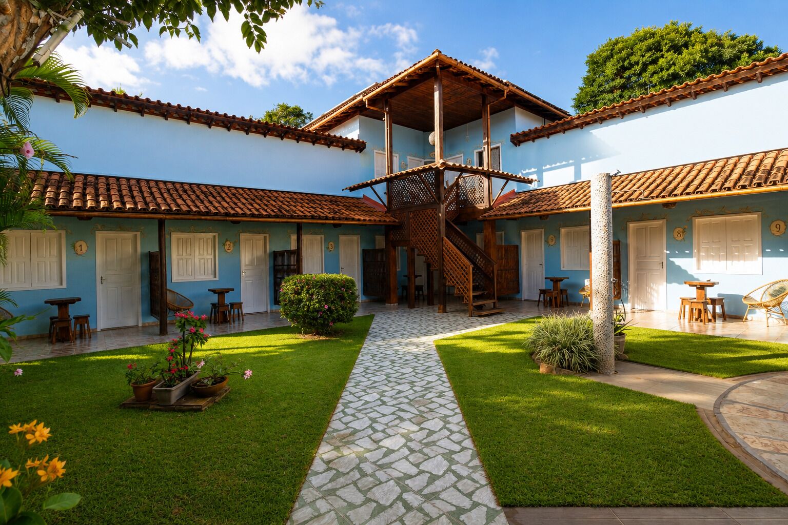 Un patio con una escalera central, rodeado por edificios de dos pisos con tejados de tejas y puertas blancas.