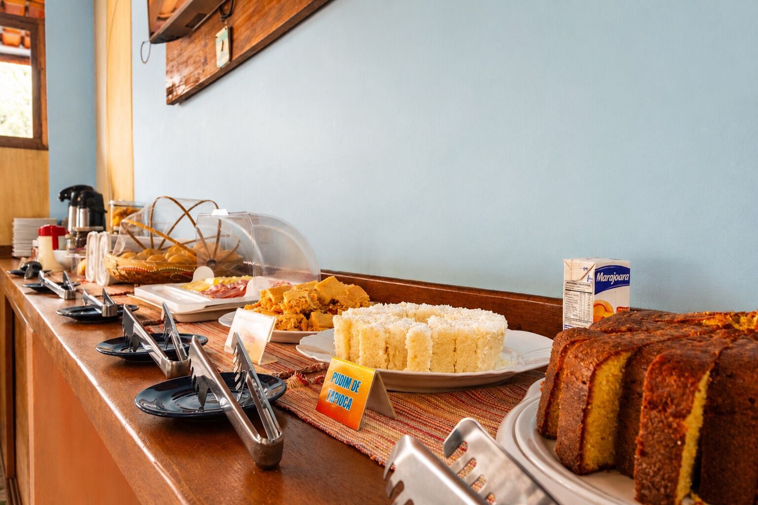 A buffet counter with various food items, including rice cakes, a loaf of bread, and a coffee machine.