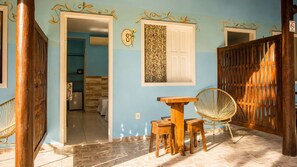 A room with a wooden table and chairs, a woven chair, a door with a number, and a patterned wall.