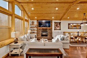 A cozy living room with a fireplace, wooden ceiling, and large windows. - Luxury Morning Star Log Cabin | Hot Tub, Firepit, Game Room & Minutes to Skiing (Big Bear Lake)