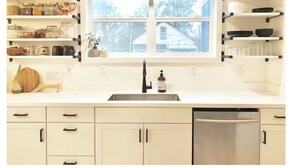 A kitchen with white cabinets, a stainless steel dishwasher, and shelves with kitchenware. - Hip & Historic downtown Vancouver bungalow (Vancouver)